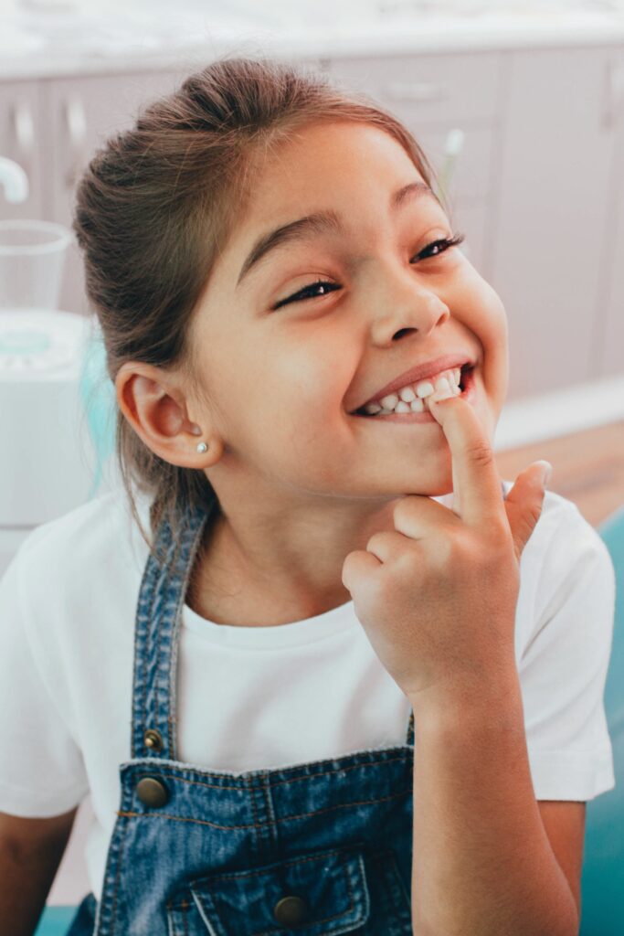 Child in dentist chair pointing to her teeth