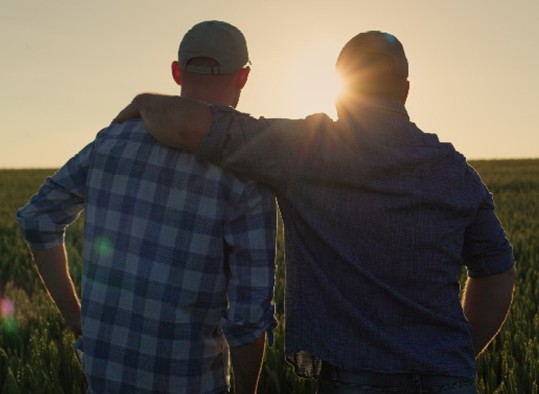 father and son facing sunset with dad's arm around son