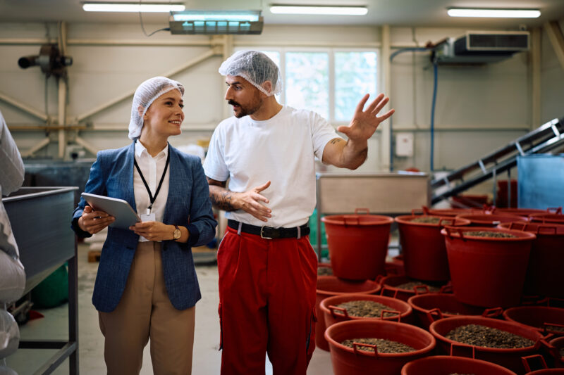 Food processing plant worker communicating with quality control inspector while walking through storage compartment.