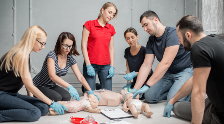 Group people watch instructor do CPR on infant mannequin