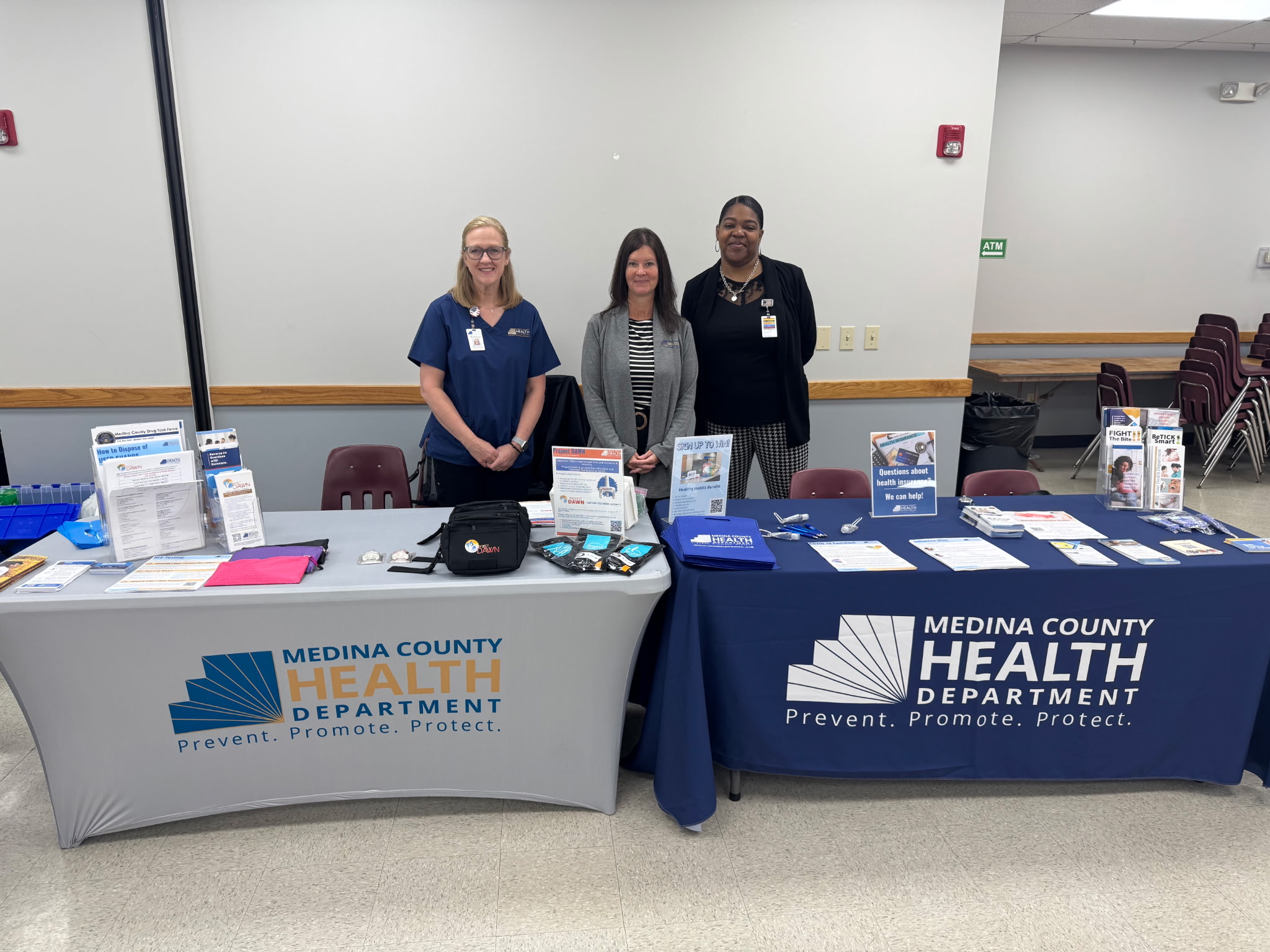 3 women standing behind a table that holds information about the health department